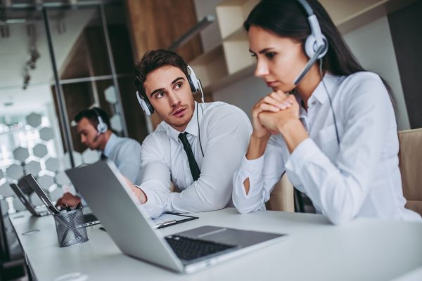 How can I help you? Beautiful call center workers in headphones are working at modern office.